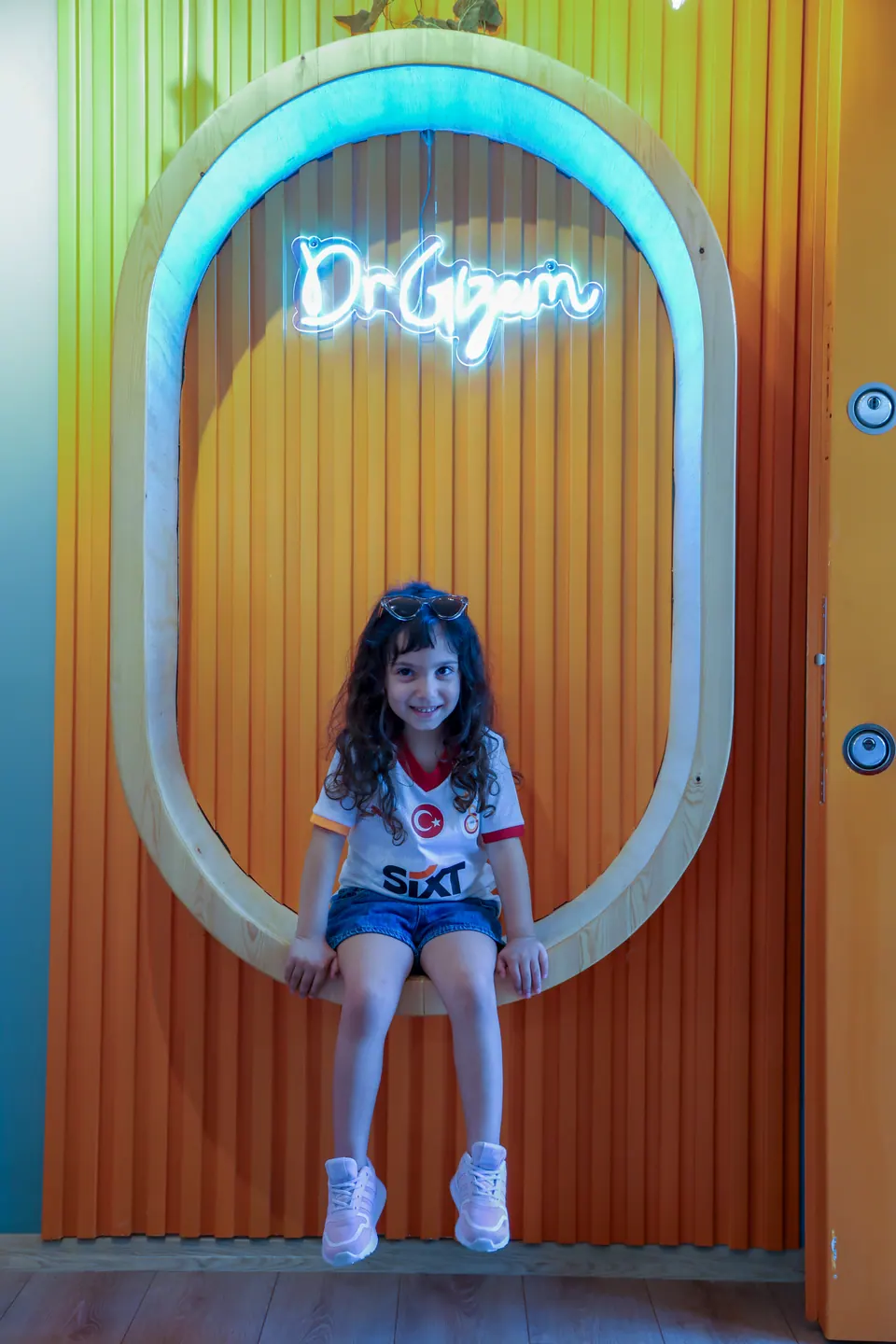 Turuncu duvardaki neon ışıklı oval çerçevede gülümseyen kız çocuğu