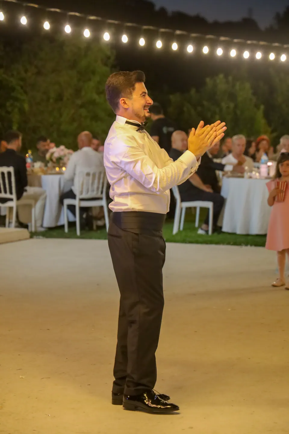 Işık zincirleri altındaki bahçe düğününde alkışlayan damat