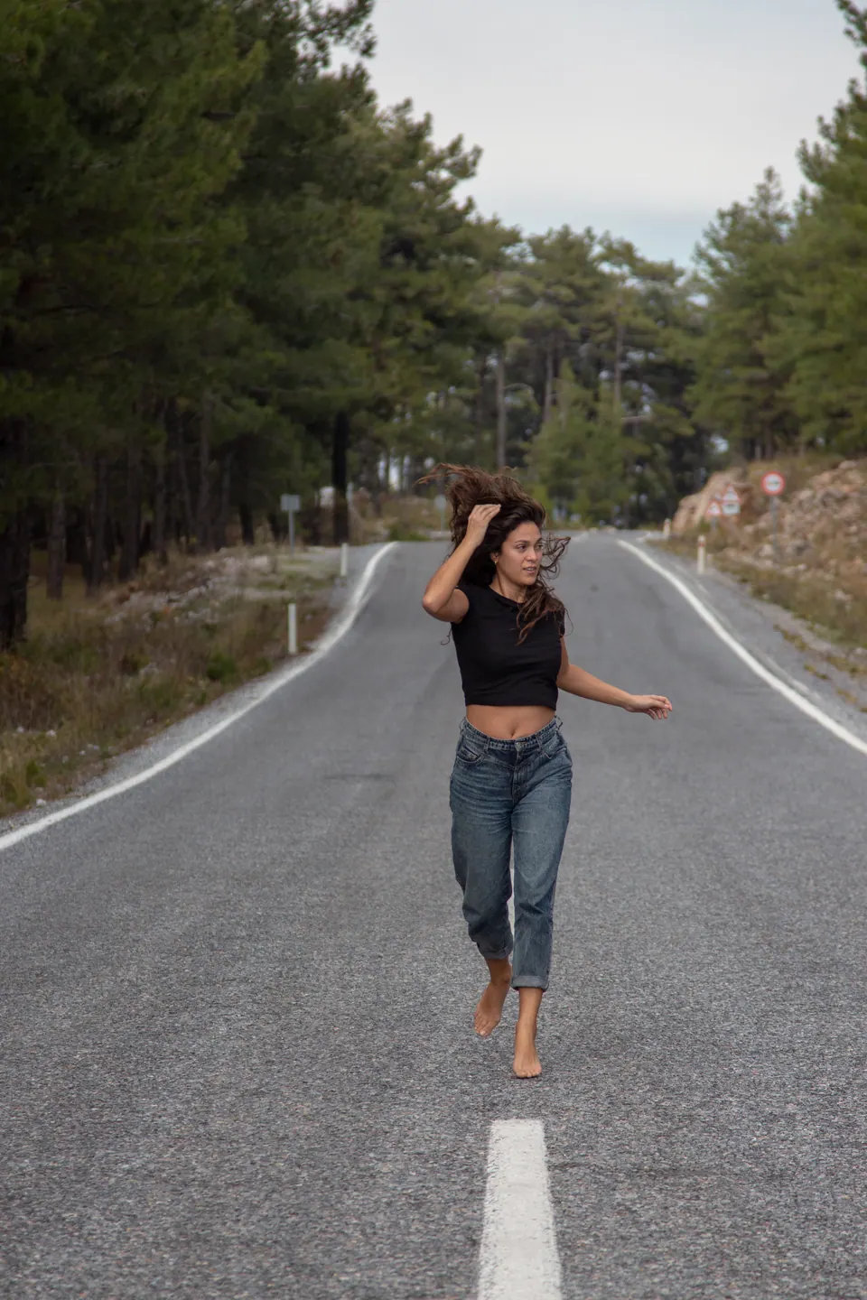 Çam ağaçlı yolda yalınayak koşan kot pantolonlu model
