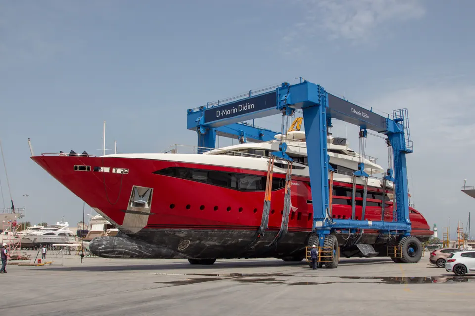 Tersane sahasında travel lift ile taşınan kırmızı süper yatın geniş açı çekimi