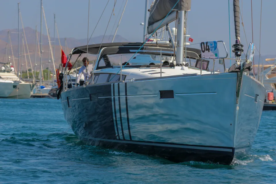 Yarış numaralı yelkenli yatın marinadan ayrılışı, dağlar arka planda